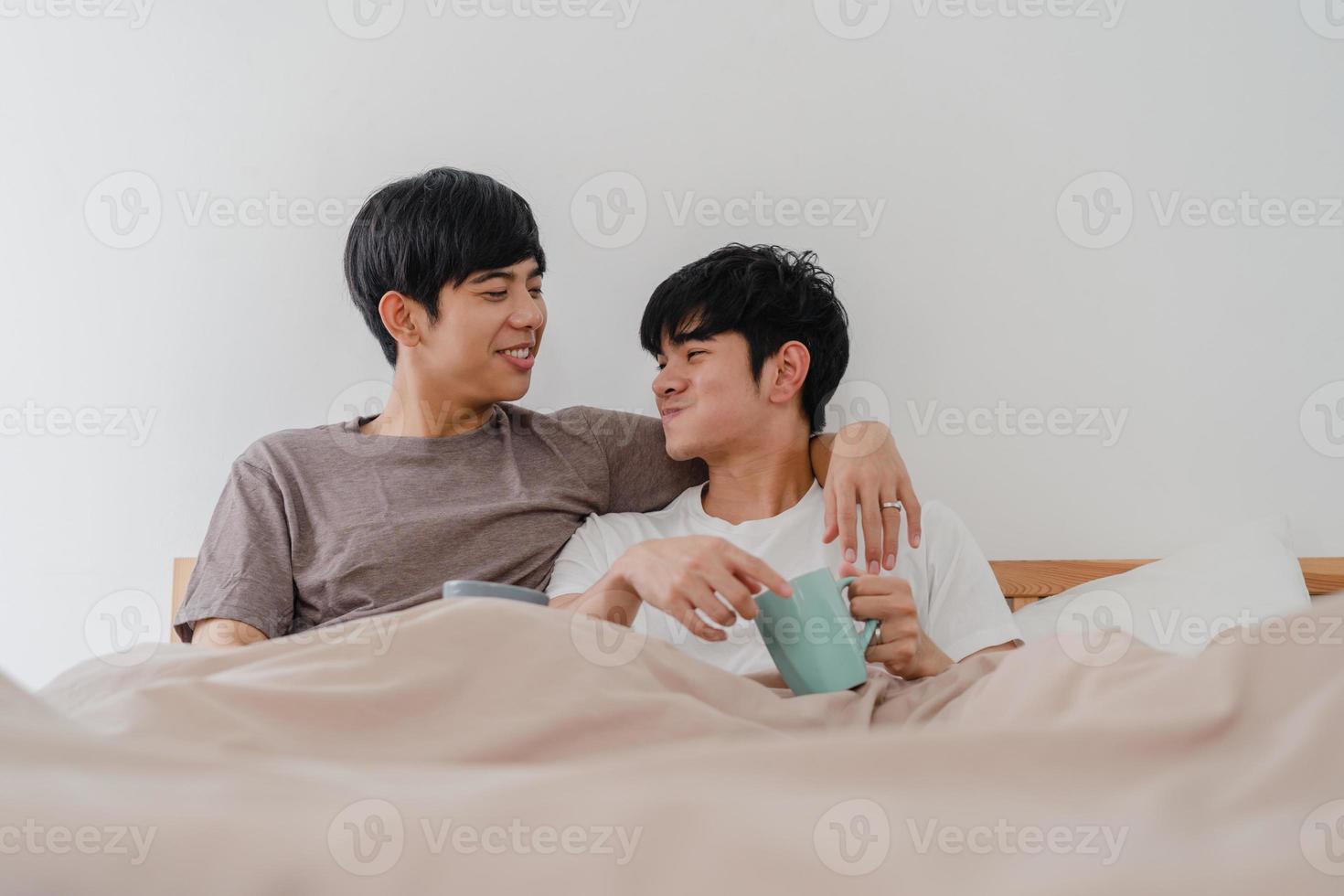 Asian Gay men couple talking having a great time at modern home. Young Asia lover male happy relax rest drink coffee after wake up while lying on bed in bedroom at house in the morning concept. photo