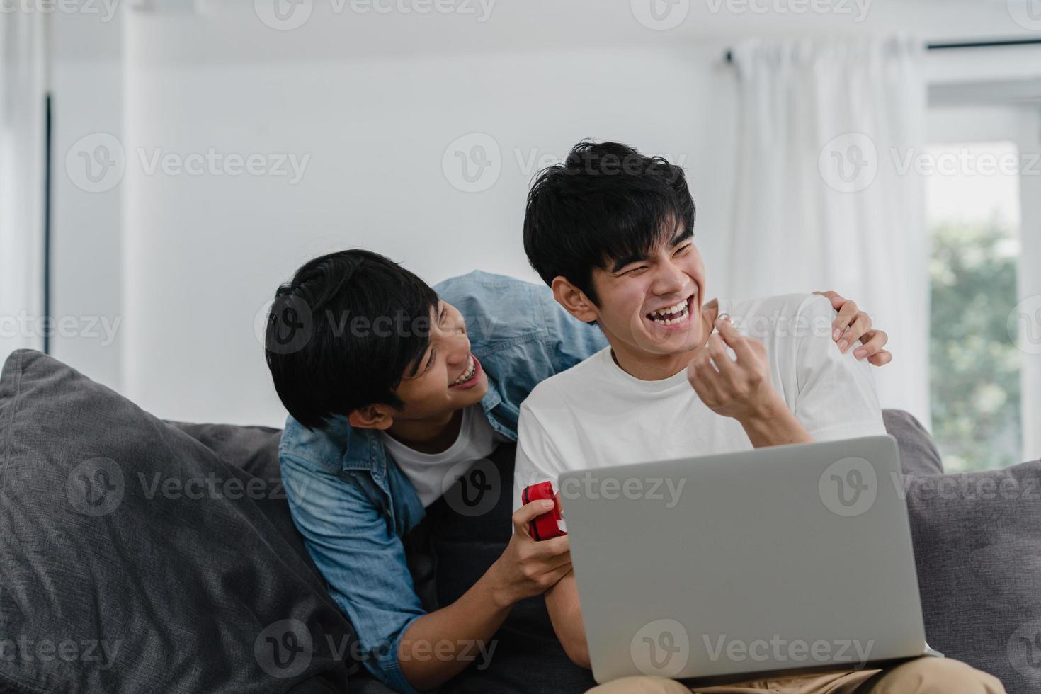 Young Asian gay couple propose at modern home, Teen korean LGBTQ men happy smiling have romantic time while proposing and marriage surprise wear wedding ring in living room at house concept. photo