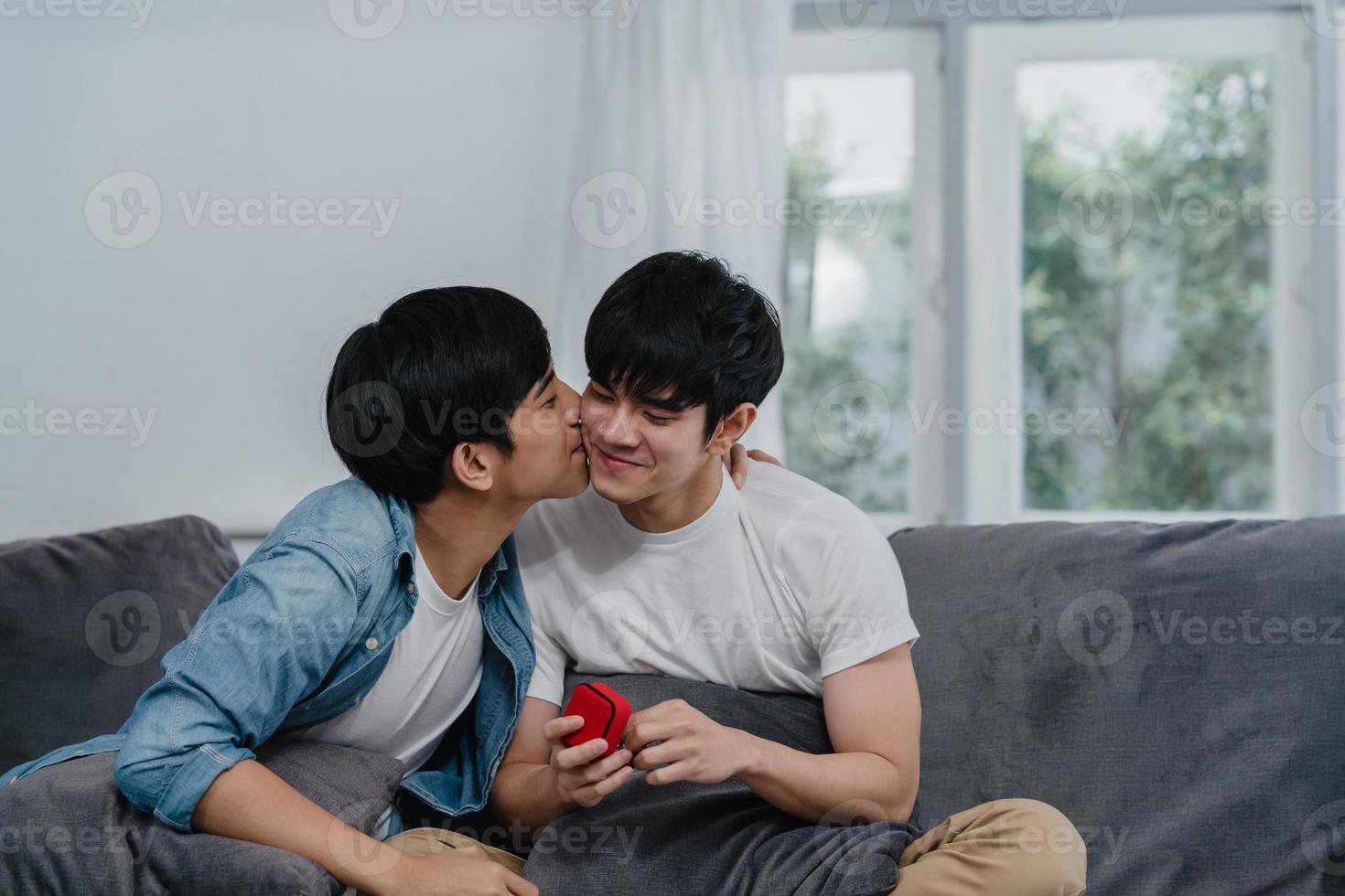 joven pareja gay asiática proponer en casa, hombres lgbtq coreanos adolescentes felices sonriendo tienen tiempo romántico mientras proponen y matrimonio sorpresa usan anillo de bodas en la sala de estar en el concepto de casa. foto