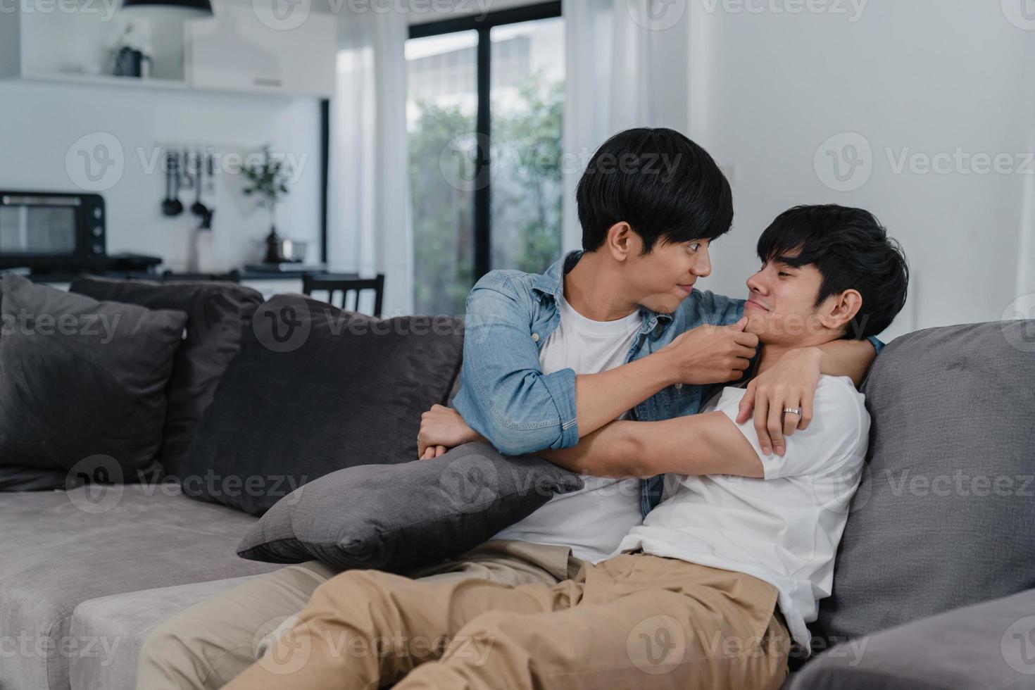 Young Asian Gay couple hug and kiss at home. Attractive Asian LGBTQ pride men happy relax spend romantic time together while lying sofa in living room concept. photo