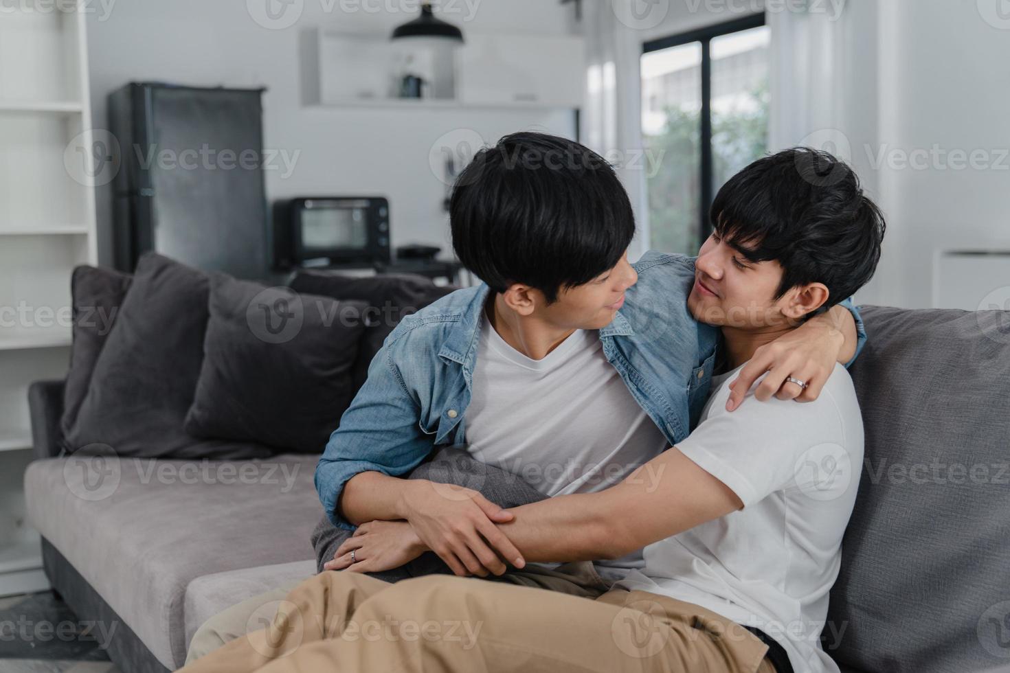 Young Asian Gay couple hug and kiss at home. Attractive Asian LGBTQ pride men happy relax spend romantic time together while lying sofa in living room concept. photo