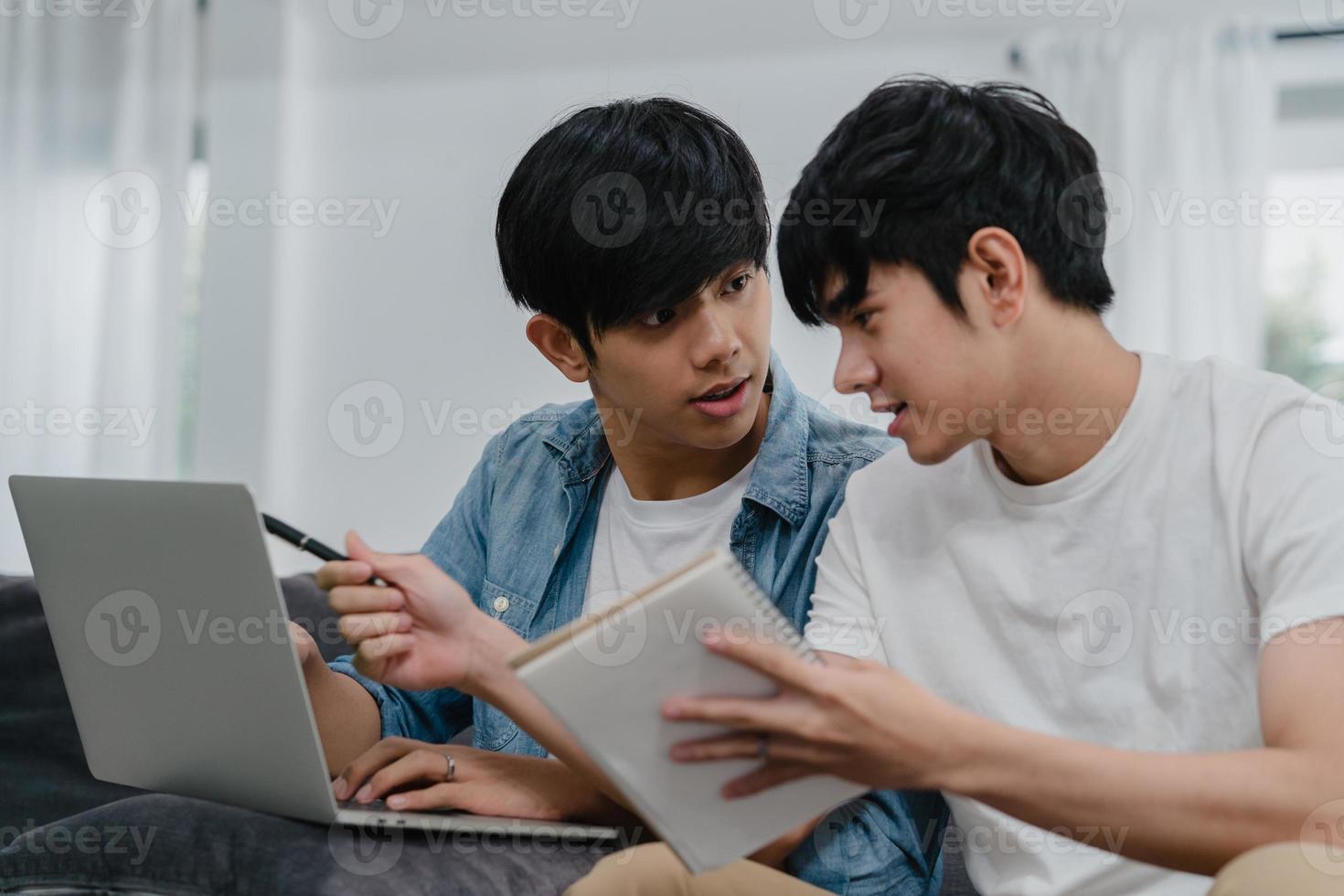 Young Asian Gay couple working laptop at modern home. Asia LGBTQ men happy relax fun using computer and analyzing their finances in internet together while lying sofa in living room at house concept. photo