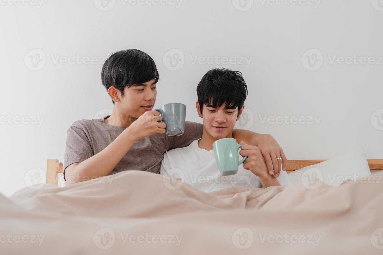 Asian Gay men couple talking having a great time at modern home. Young Asia lover male happy relax rest drink coffee after wake up while lying on bed in bedroom at house in the morning concept. photo
