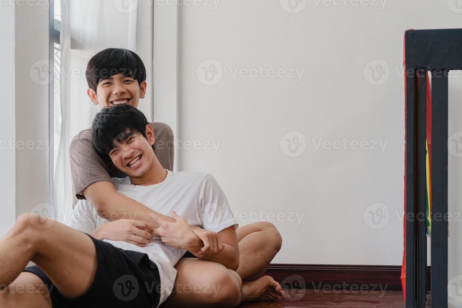 Asian Gay couple lying and hugging on the floor at home. Young Asian LGBTQ men kissing happy relax rest together spend romantic time in living room with rainbow flag at modern house in the morning. photo