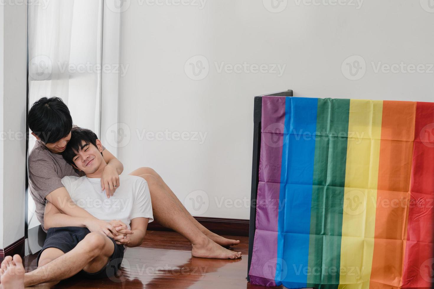 Asian Gay couple lying and hugging on the floor at home. Young Asian LGBTQ men kissing happy relax rest together spend romantic time in living room with rainbow flag at modern house in the morning. photo