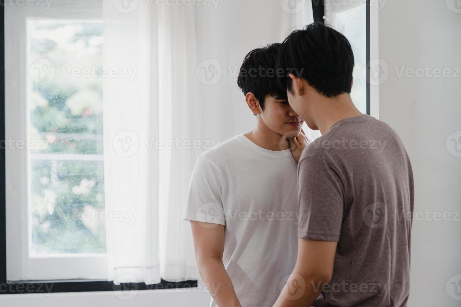 Pareja gay asiática de pie y abrazándose cerca de la ventana en casa. Hombres jóvenes asiáticos lgbtq besándose felices relajarse descansar juntos pasar tiempo romántico en la sala de estar de la casa moderna en el concepto de la mañana. foto