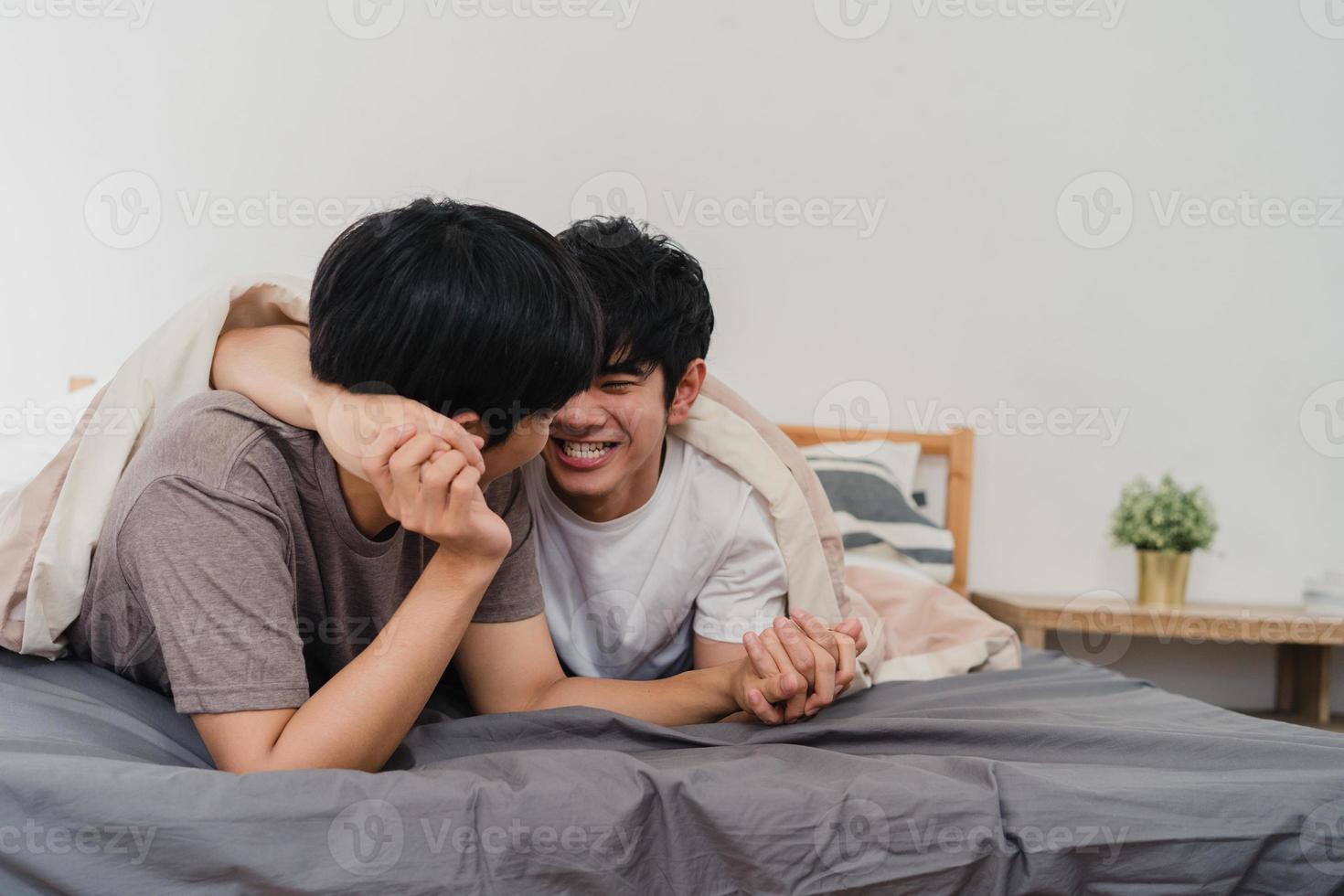 Handsome Asian gay couple talking on bed at home. Young Asian LGBTQ guy happy relax rest together spend romantic time after wake up in bedroom at modern house in the morning concept. photo