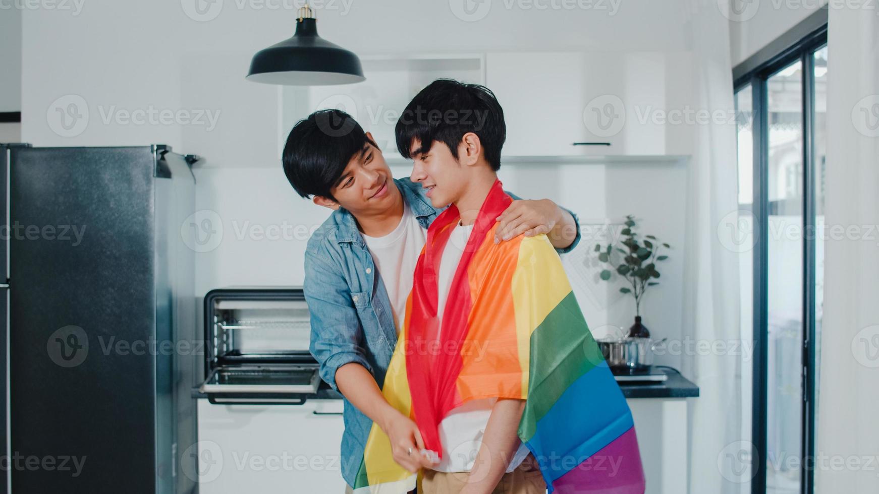 Asian Gay couple standing and hugging room at home. Young handsome LGBTQ men kissing happy relax rest together spend romantic time in modern kitchen with rainbow flag at house in the morning concept. photo