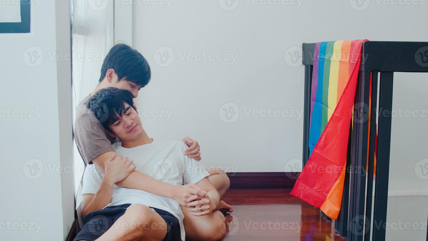 Asian Gay couple lying and hugging on the floor at home. Young Asian LGBTQ men kissing happy relax rest together spend romantic time in living room with rainbow flag at modern house in the morning. photo