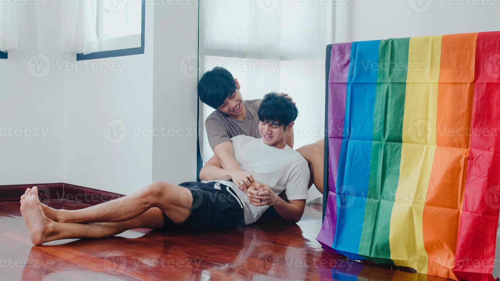 Asian Gay couple lying and hugging on the floor at home. Young Asian LGBTQ men kissing happy relax rest together spend romantic time in living room with rainbow flag at modern house in the morning. photo