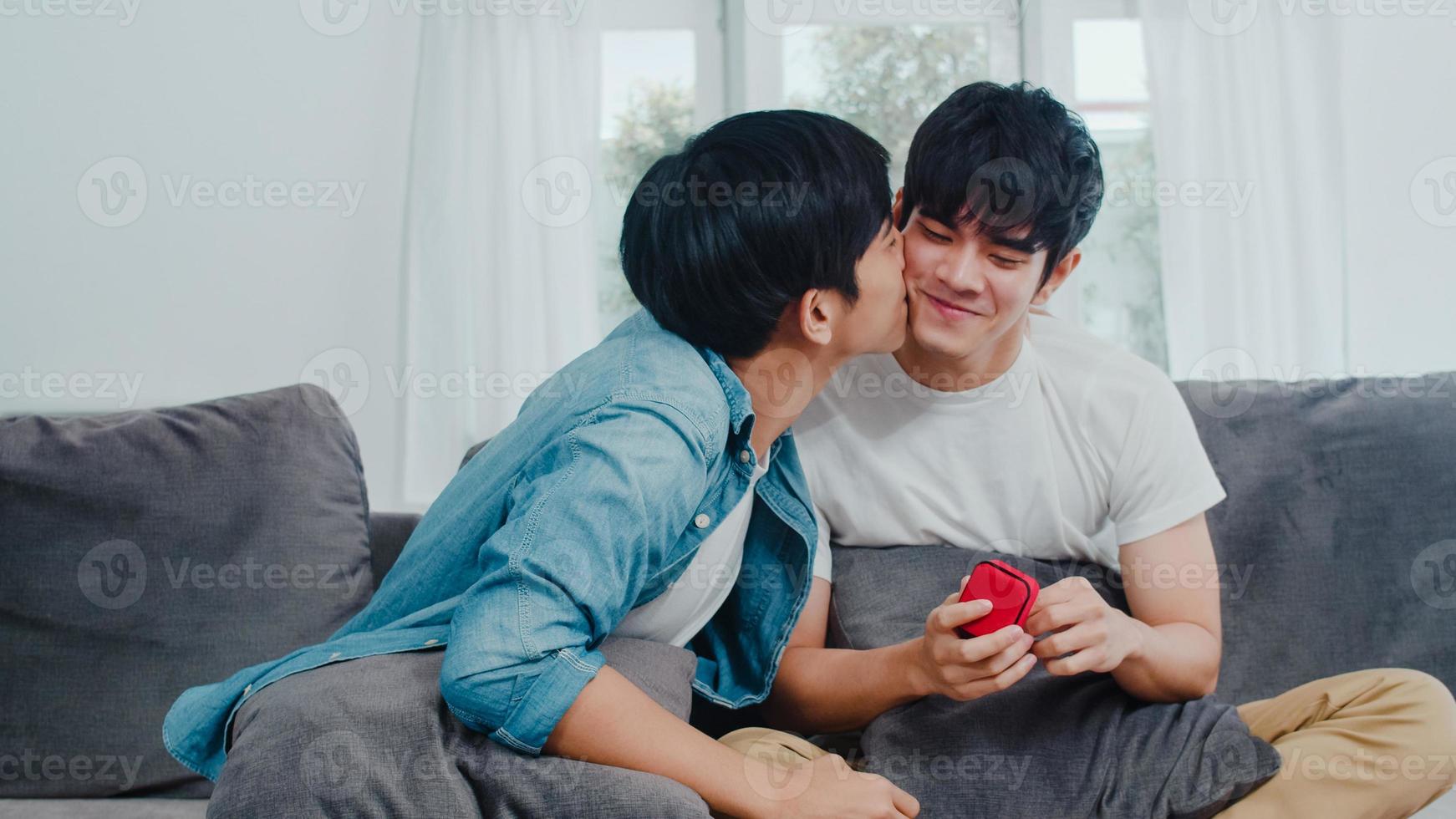 joven pareja gay asiática proponer en casa, hombres lgbtq coreanos adolescentes felices sonriendo tienen tiempo romántico mientras proponen y matrimonio sorpresa usan anillo de bodas en la sala de estar en el concepto de casa. foto