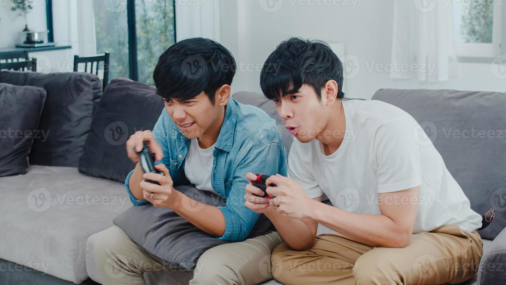 Young Asian gay couple play games at home, Teen korean LGBTQ men using joystick having funny happy moment together on sofa in living room at house. photo