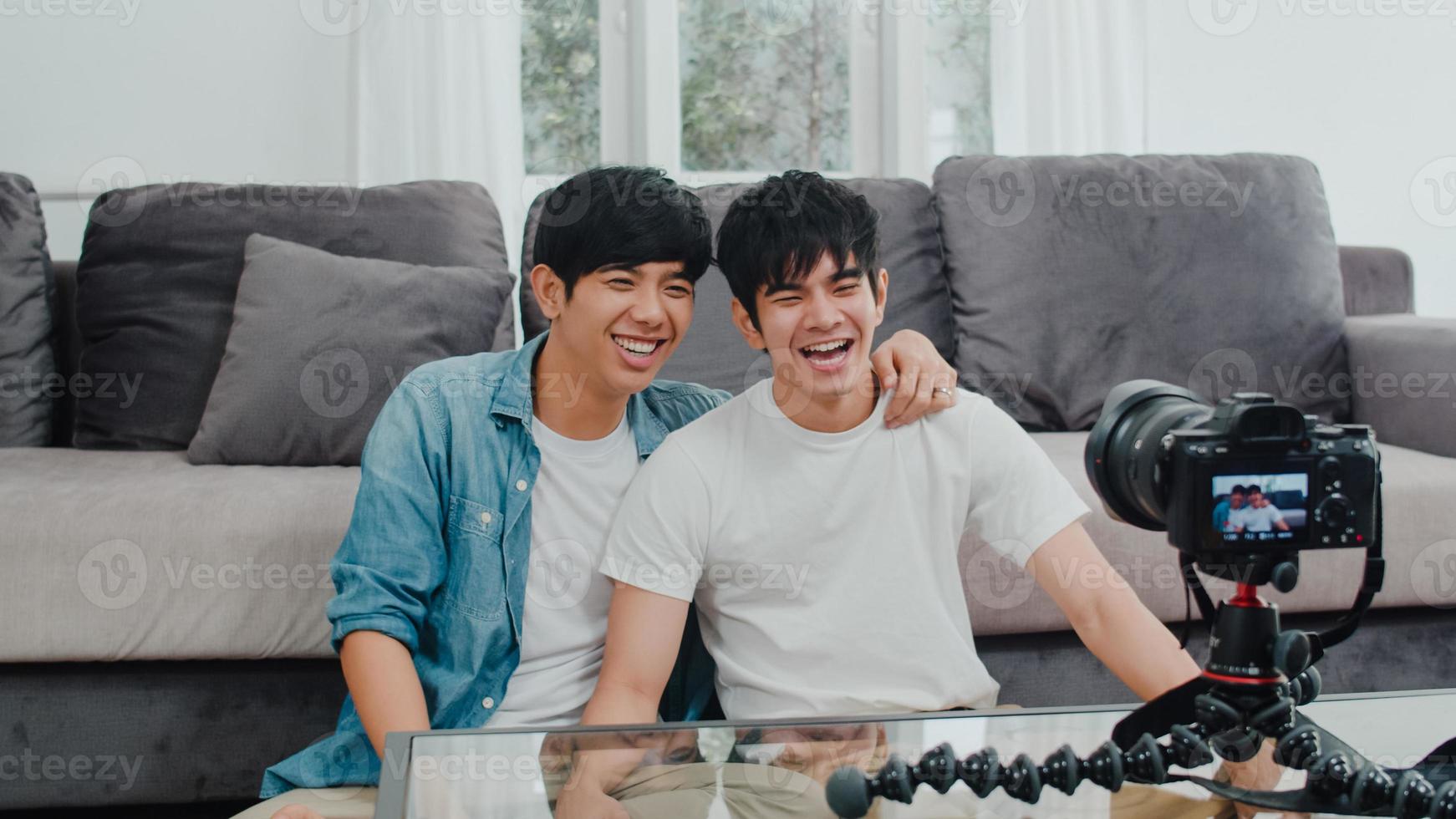 Young Asian gay couple influencer couple vlog at home. Teen korean LGBTQ men happy relax fun using camera record vlog video upload in social media while lying sofa in living room at house concept. photo