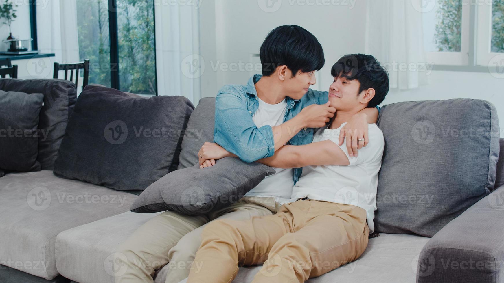 Young Asian Gay couple hug and kiss at home. Attractive Asian LGBTQ pride men happy relax spend romantic time together while lying sofa in living room concept. photo
