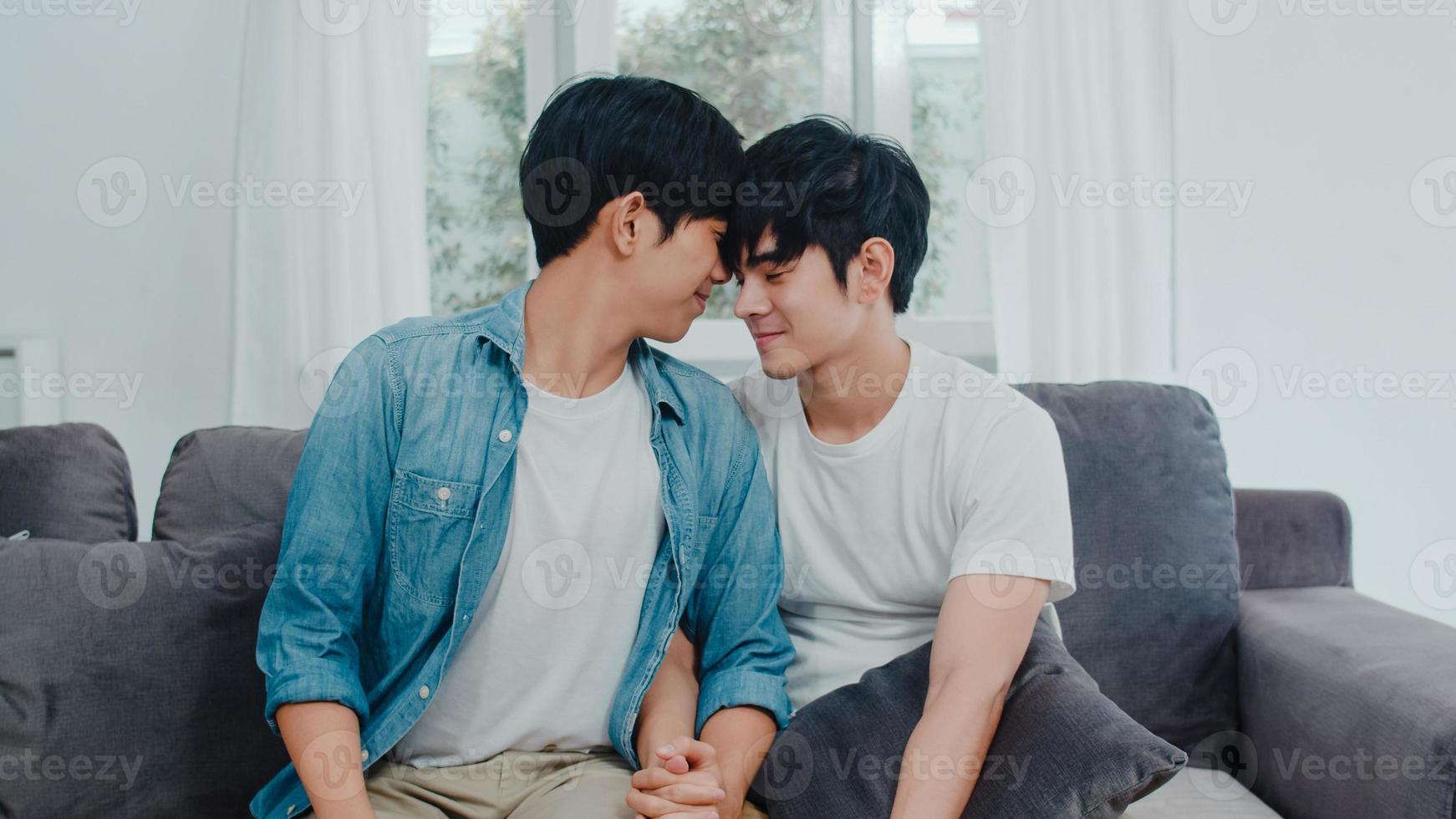 Young Asian Gay couple hug and kiss at home. Attractive Asian LGBTQ pride men happy relax spend romantic time together while lying sofa in living room concept. photo