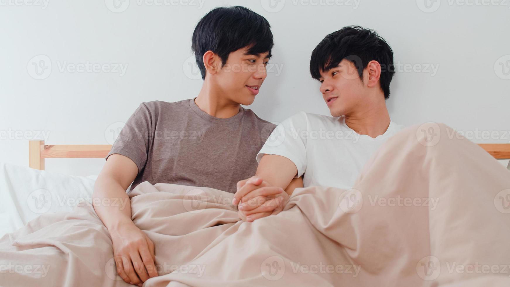 Handsome Asian gay couple talking on bed at home. Young Asian LGBTQ guy happy relax rest together spend romantic time after wake up in bedroom at modern house in the morning concept. photo