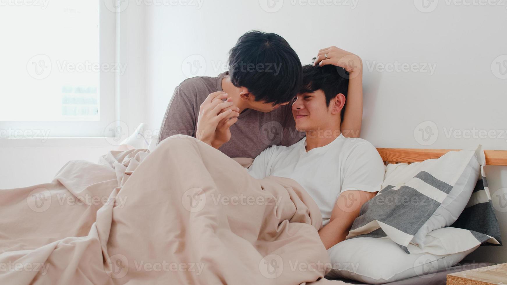 Handsome Asian gay couple talking on bed at home. Young Asian LGBTQ guy happy relax rest together spend romantic time after wake up in bedroom at modern house in the morning concept. photo