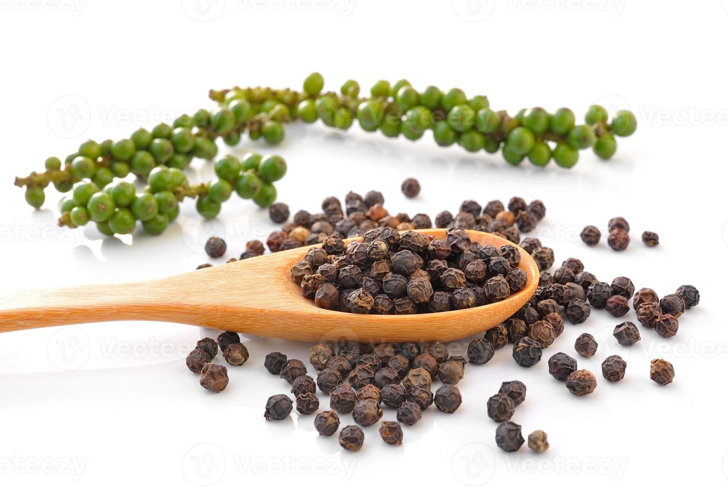 Cuchara con gránulos de pimienta negra entera y racimos de pimiento verde fresco aislado sobre fondo blanco. foto