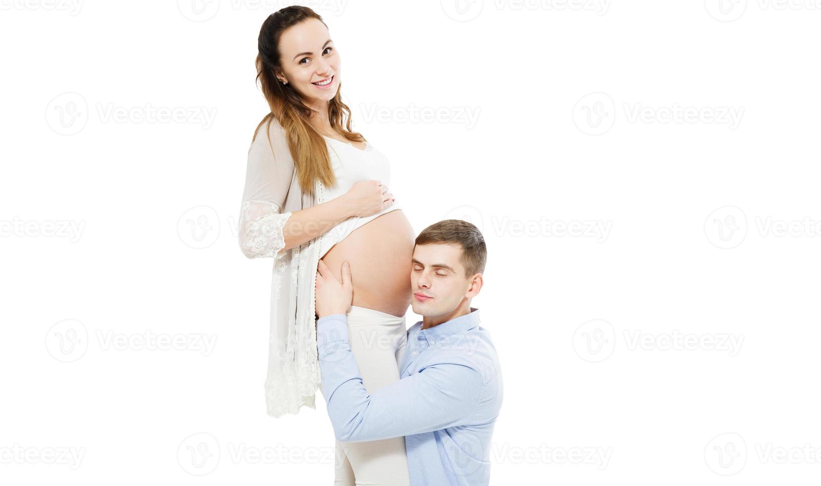 Beautiful pregnant woman and her handsome husband are smiling while spending time together. Man is listening to baby in belly photo