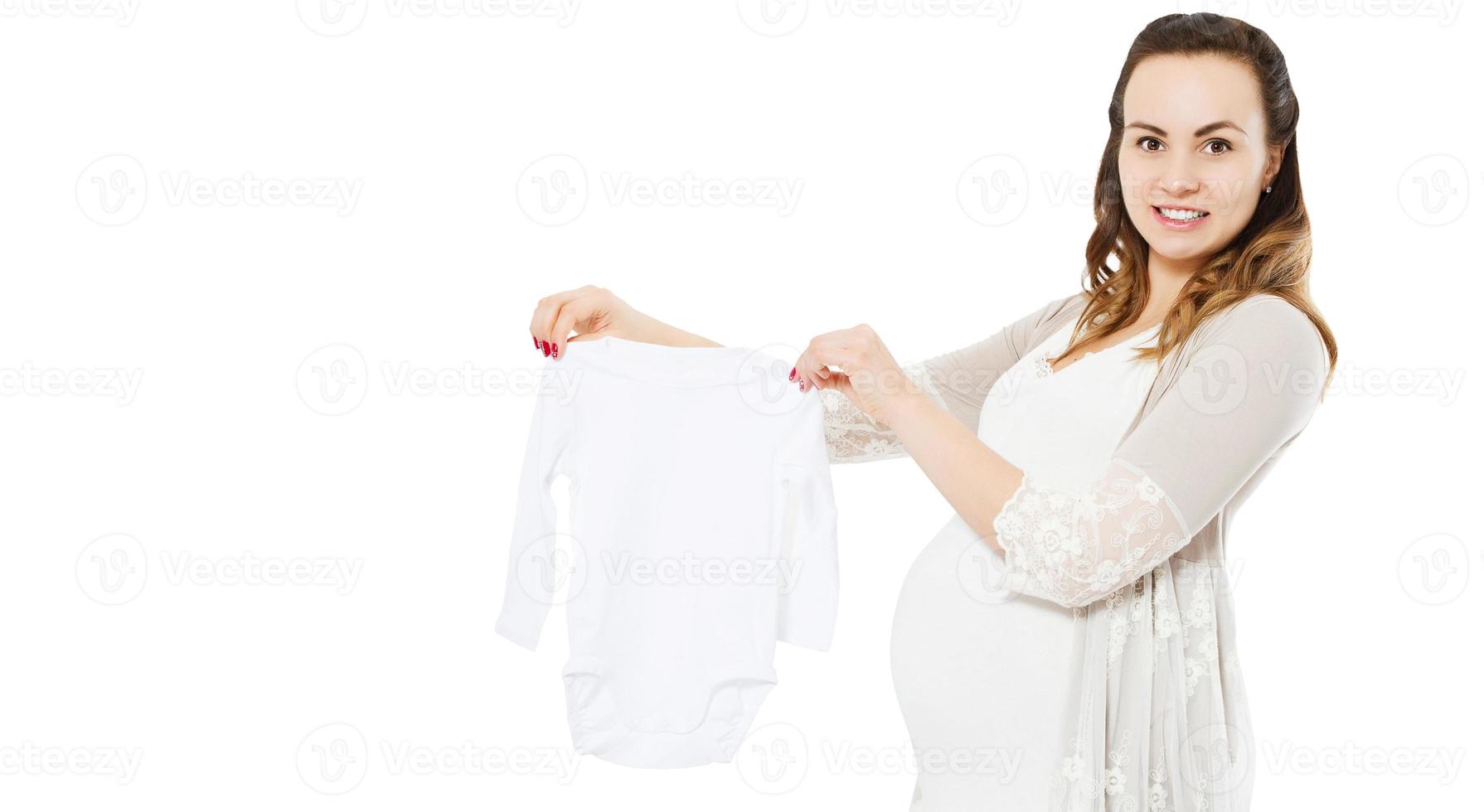 pregnant woman with belly shows baby clothes on white photo