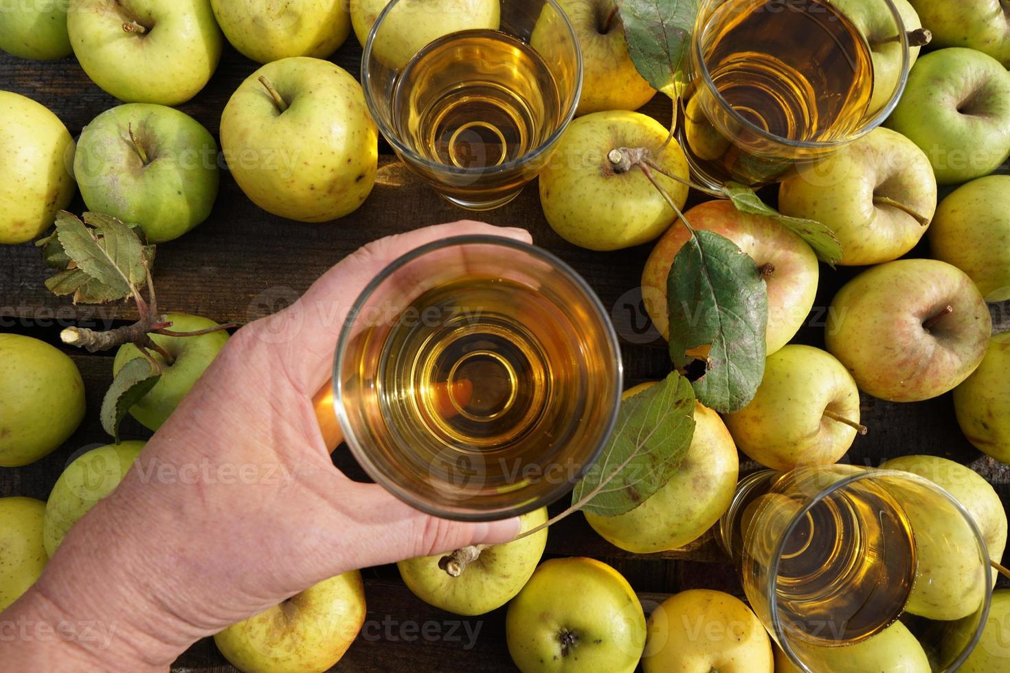 Mano femenina con un vaso de sidra de manzana y fondo de frutas amarillas. foto