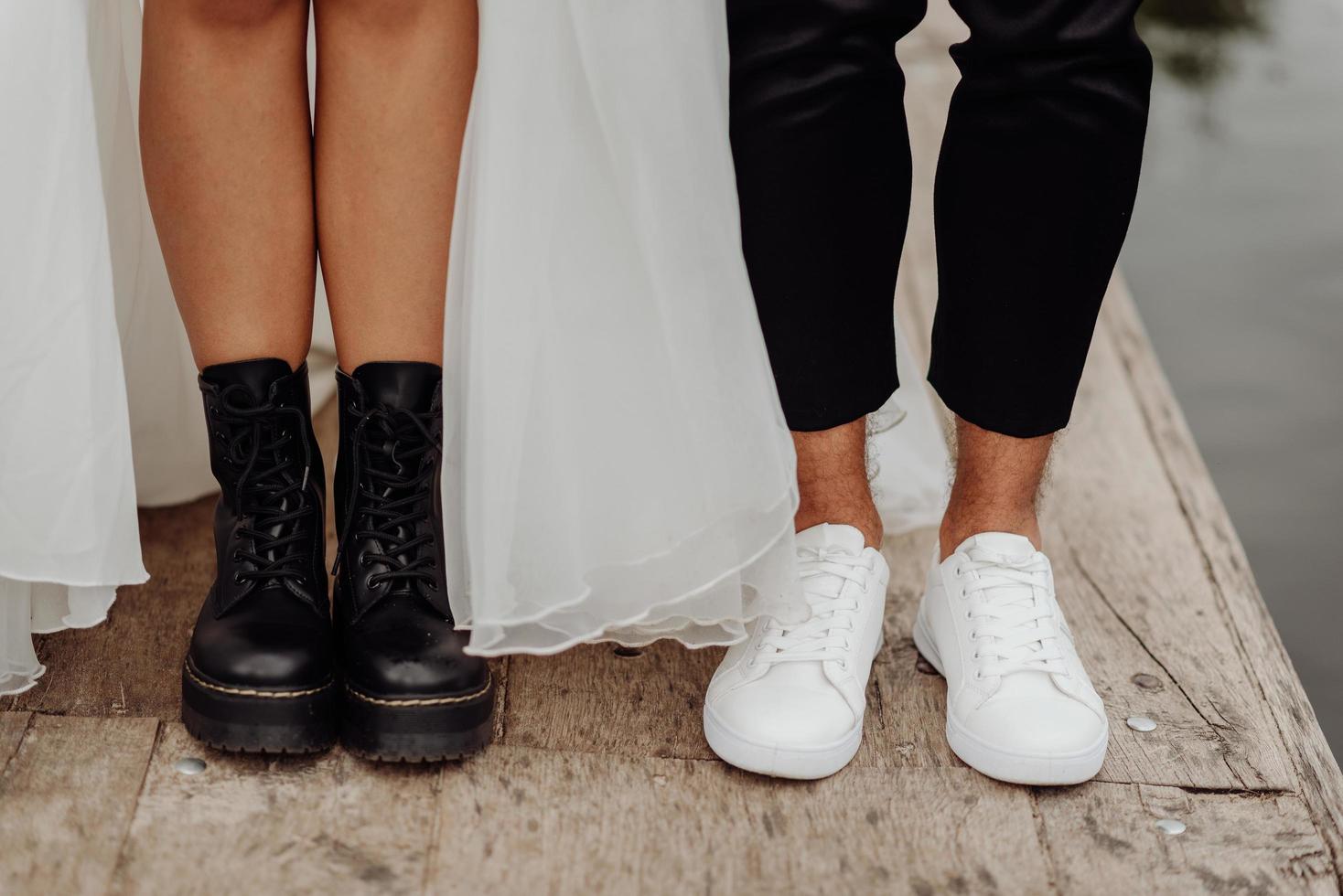 Vista frontal de los pies de la pareja de novios de pie sobre el puente de madera. Vista frontal de zapatos blancos y negros. foto