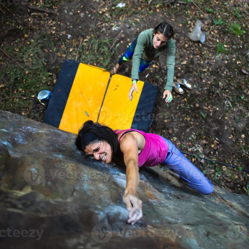 A beautiful girl practicing bouldering passes with the crash pad and her partner protecting her in the event of a fall photo