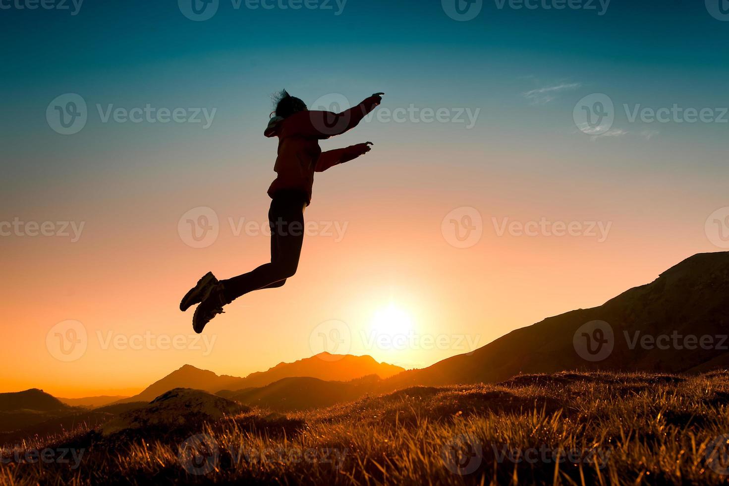 niña salta en el prado durante una puesta de sol en las montañas foto