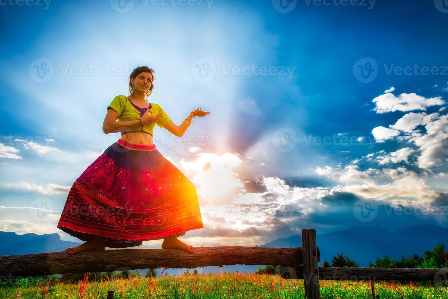 Casual girl relaxes doing stretching and yoga alone in the mountains over a fence in a beautiful spring meadow. photo