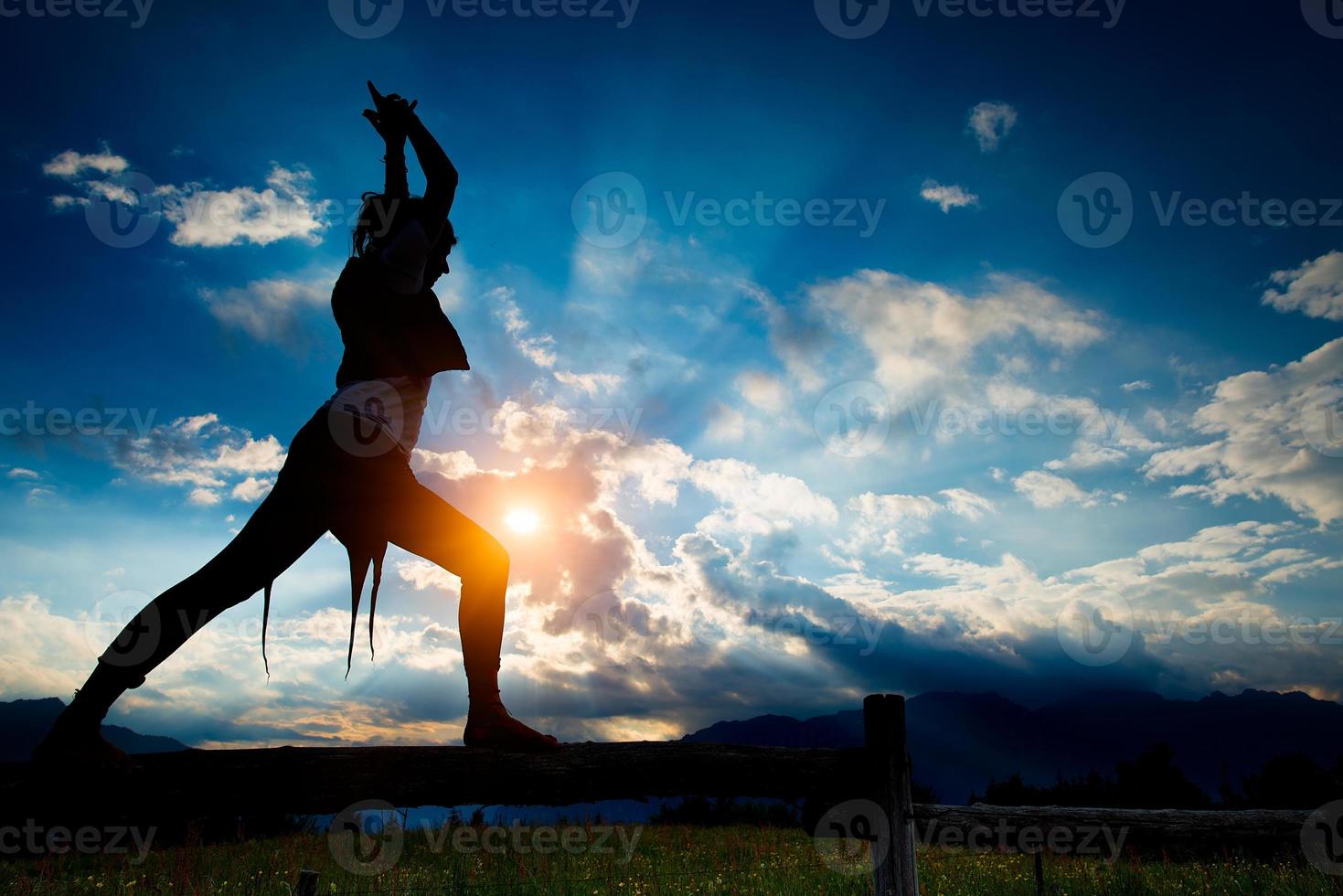 Casual girl relaxes doing stretching and yoga alone in the mountains over a fence in a beautiful spring meadow. photo