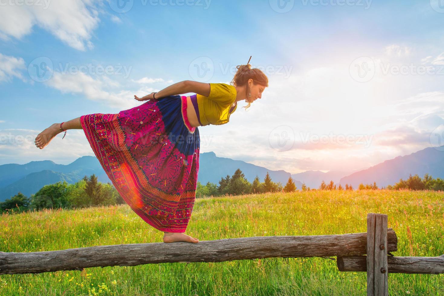 Casual girl relaxes doing stretching and yoga alone in the mountains over a fence in a beautiful spring meadow. photo