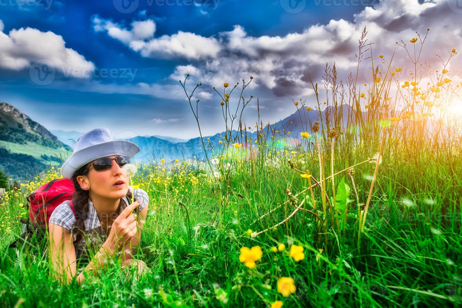 Girl in mountain meadow blowing flower photo