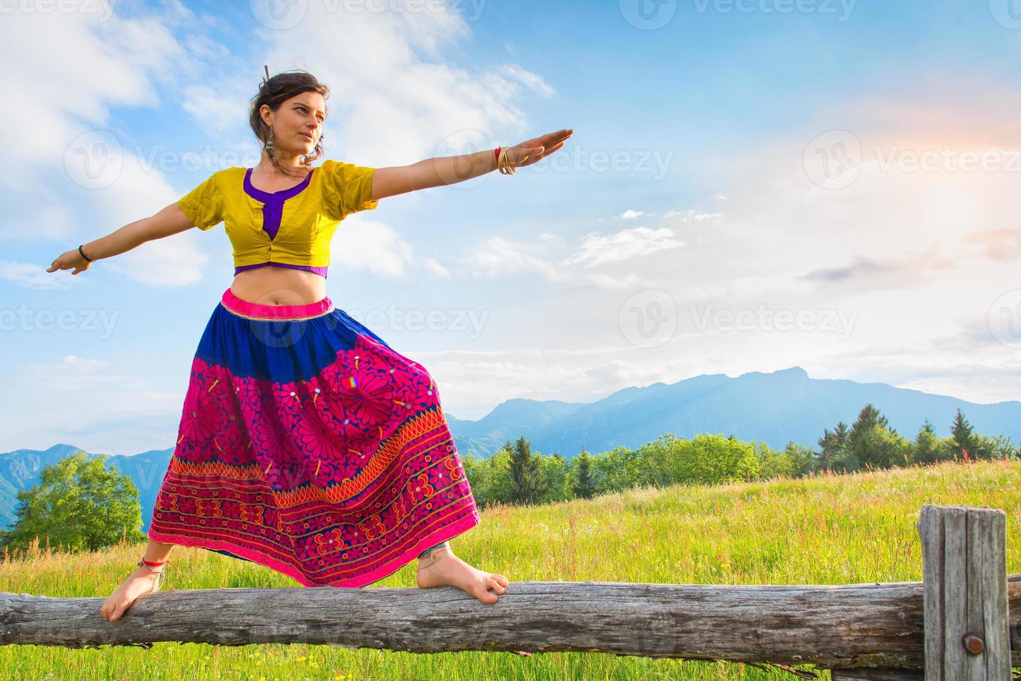 Casual girl relaxes doing stretching and yoga alone in the mountains over a fence in a beautiful spring meadow. photo