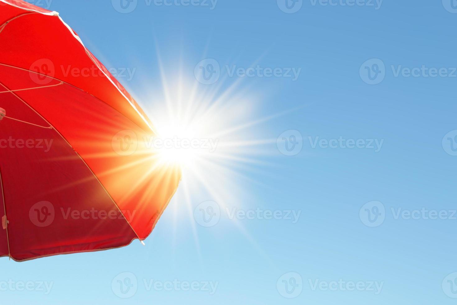 sombrilla con rayos de sol sombrilla de playa roja que protege el fuerte sol de verano en el cielo azul. foto