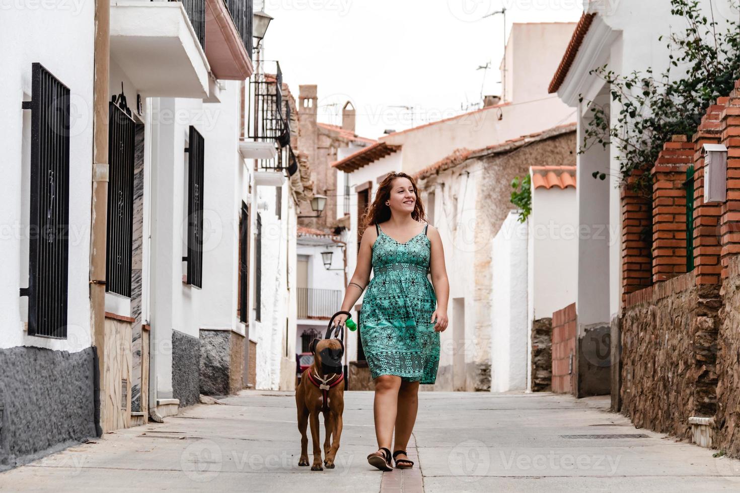 Mujer joven caminando por la calle con perro boxer foto