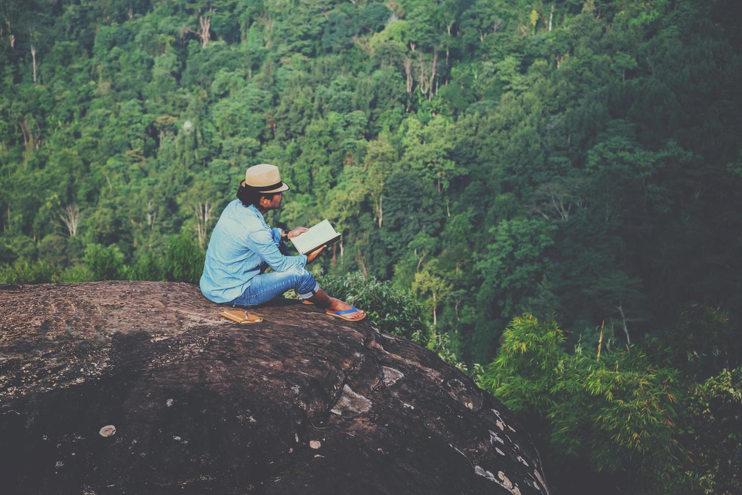 Asian man travel relax in the holiday. seats relax read books on rocky cliffs. On the Moutain. In Thailand photo