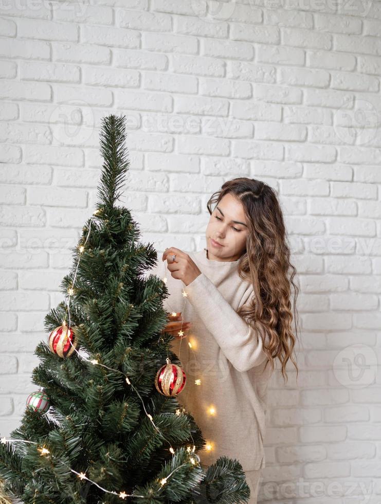 young attractive woman decorating the Christmas tree with fairy lights photo