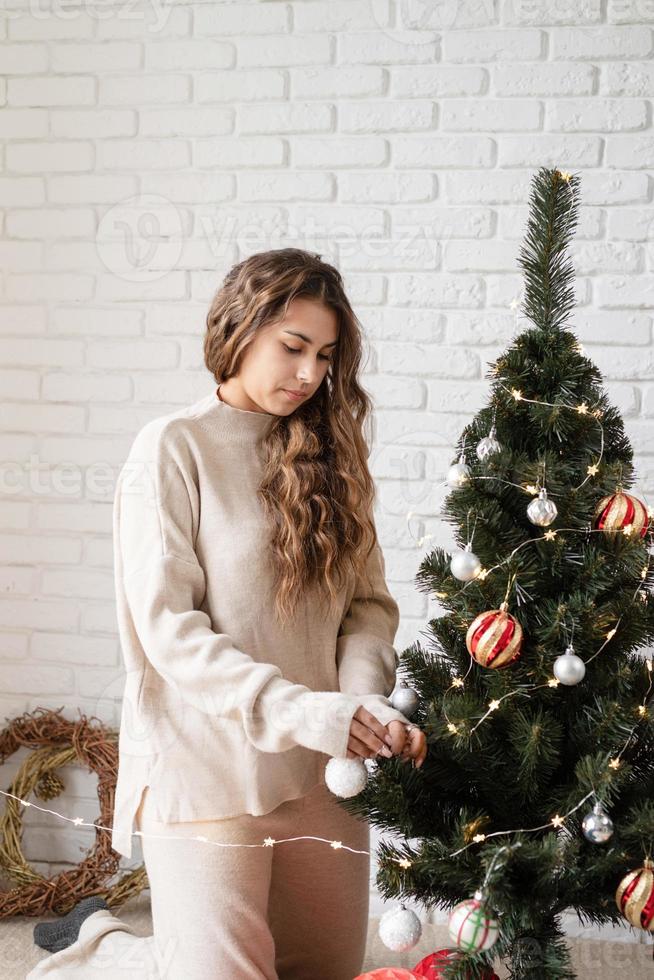 young attractive woman decorating the Christmas tree with fairy lights photo