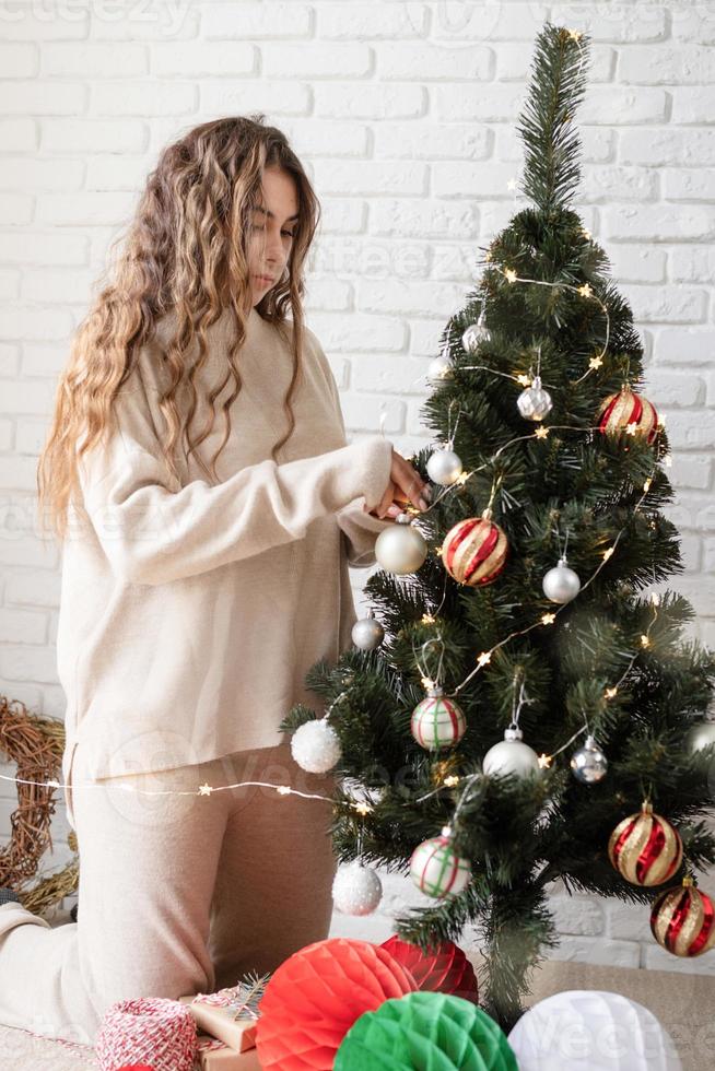 Atractiva mujer joven decorar el árbol de navidad con luces de colores foto