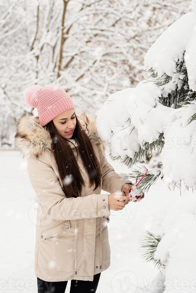 Bella mujer en ropa de abrigo de invierno decorar el árbol de navidad en un parque en un día de nieve foto