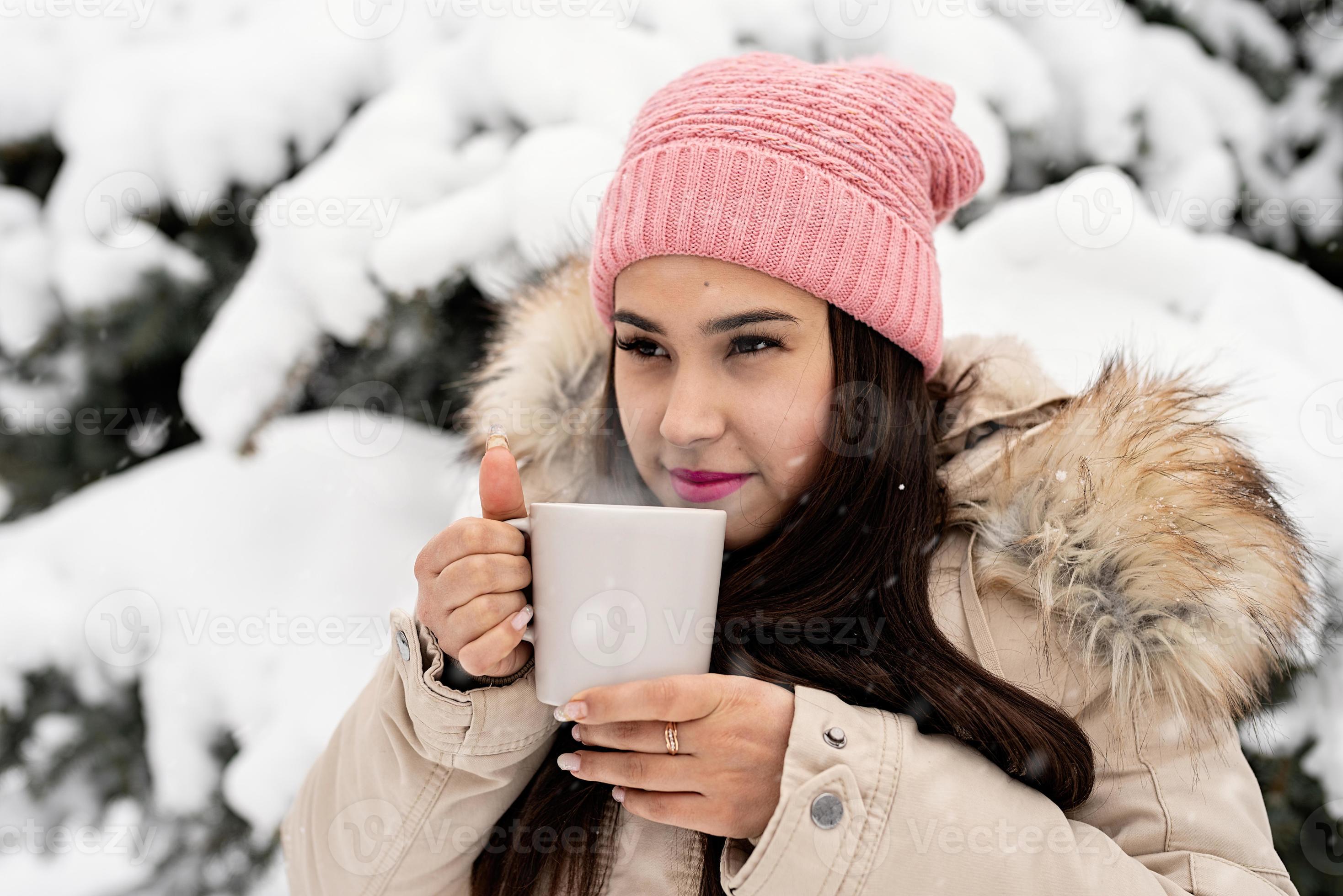 Mujer en ropa de invierno elegante con taza de café al aire libre.