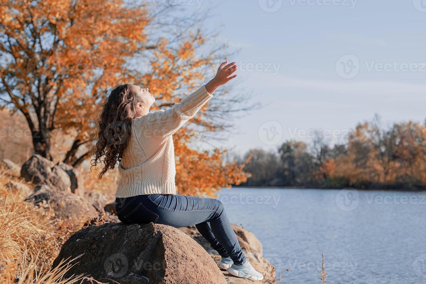 Mujer romántica pensativa sentada sobre las rocas en la orilla del río al atardecer en el día de otoño foto