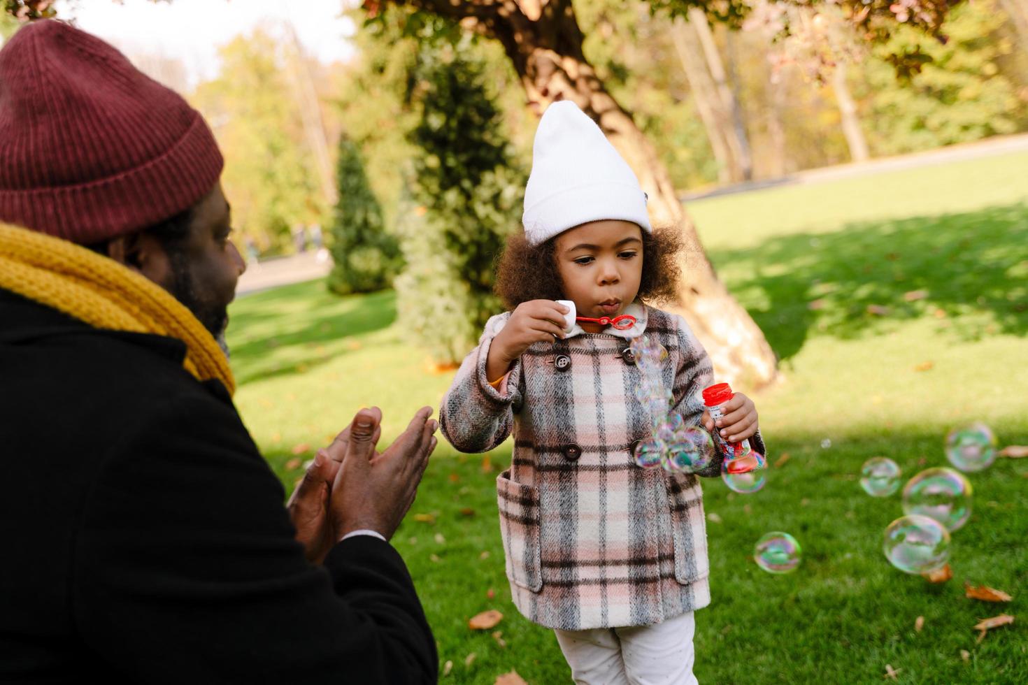 Black girl blowing soap bubbles during walking in autumn park photo