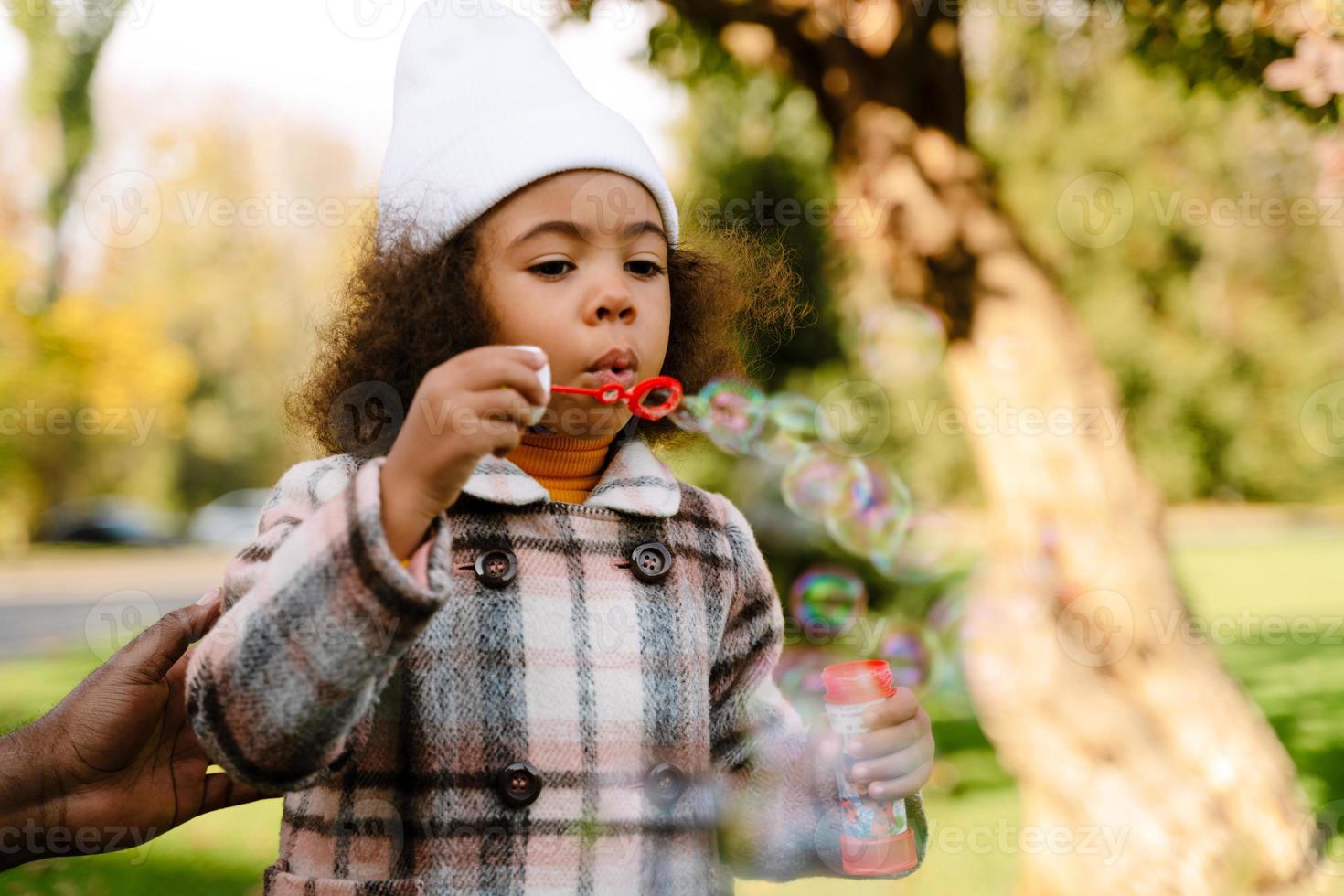 Black girl blowing soap bubbles and walking in an autumn park photo