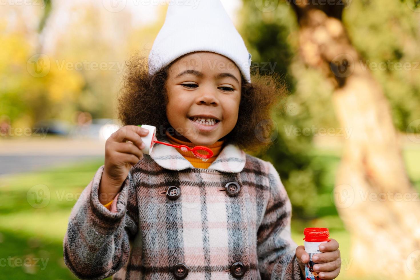 Black girl blowing soap bubbles while walking in autumn park photo