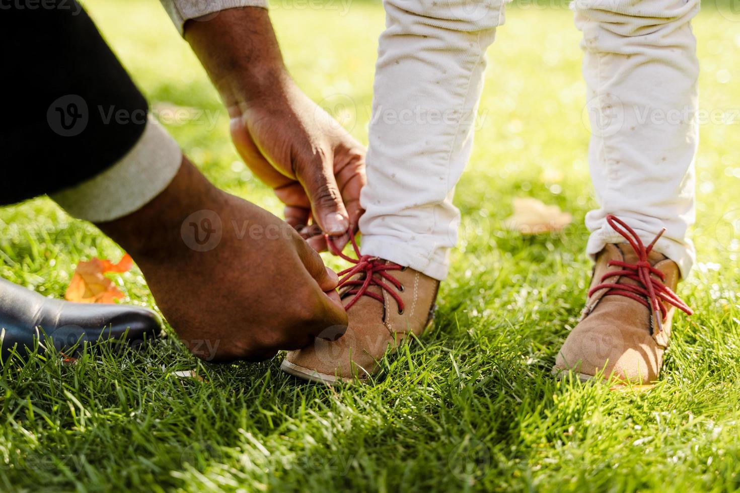 Abuelo negro atar los cordones de los zapatos de la nieta mientras camina en el parque de otoño foto