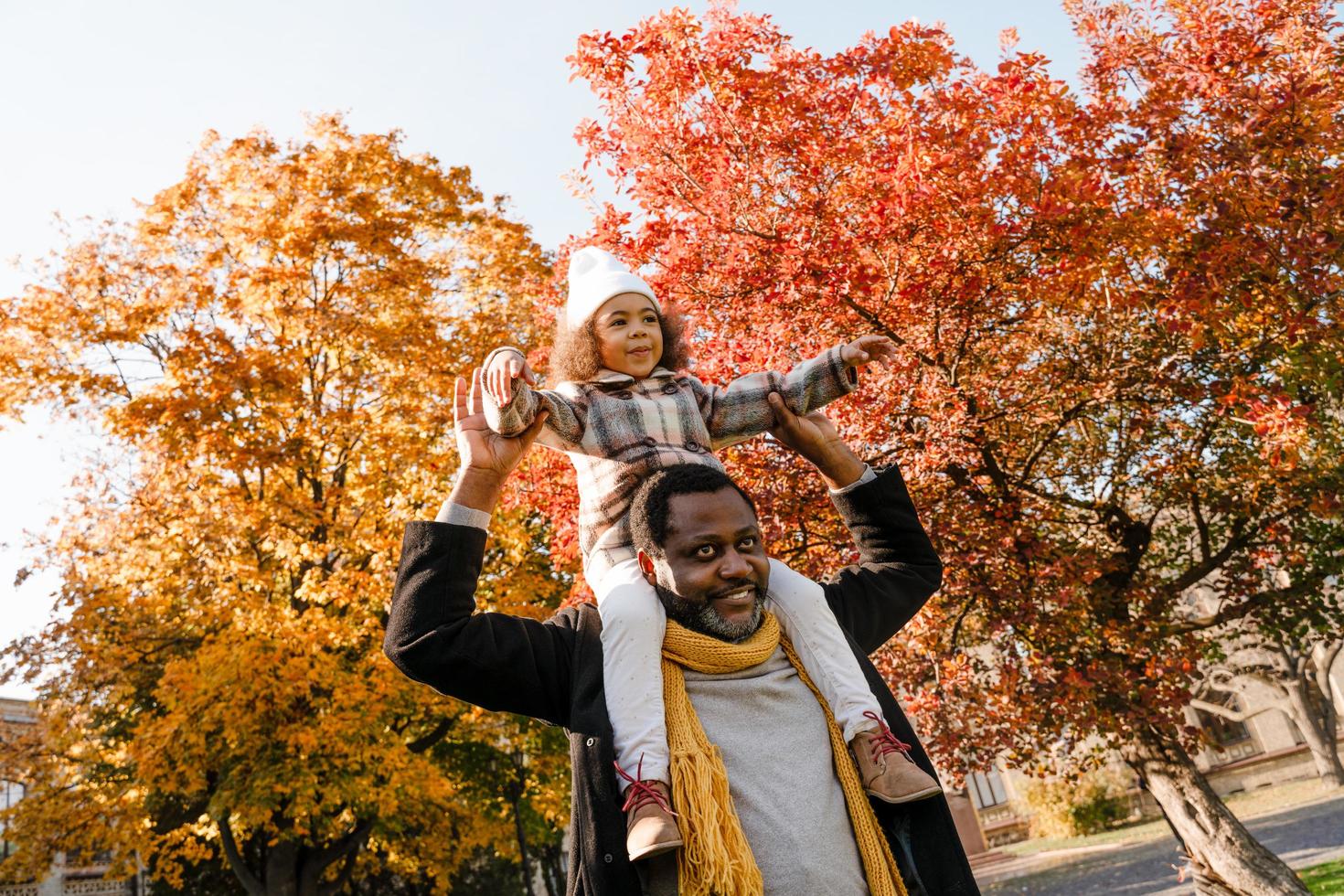 Chica negra divirtiéndose y sentada en el cuello de su abuelo en el parque de otoño foto