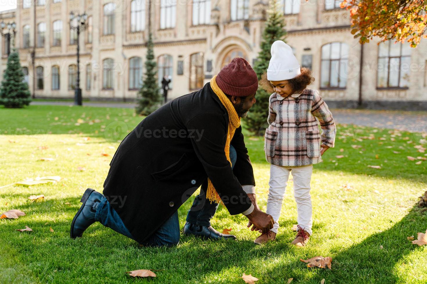 Abuelo negro atar los cordones de los zapatos de la nieta mientras camina en el parque de otoño foto