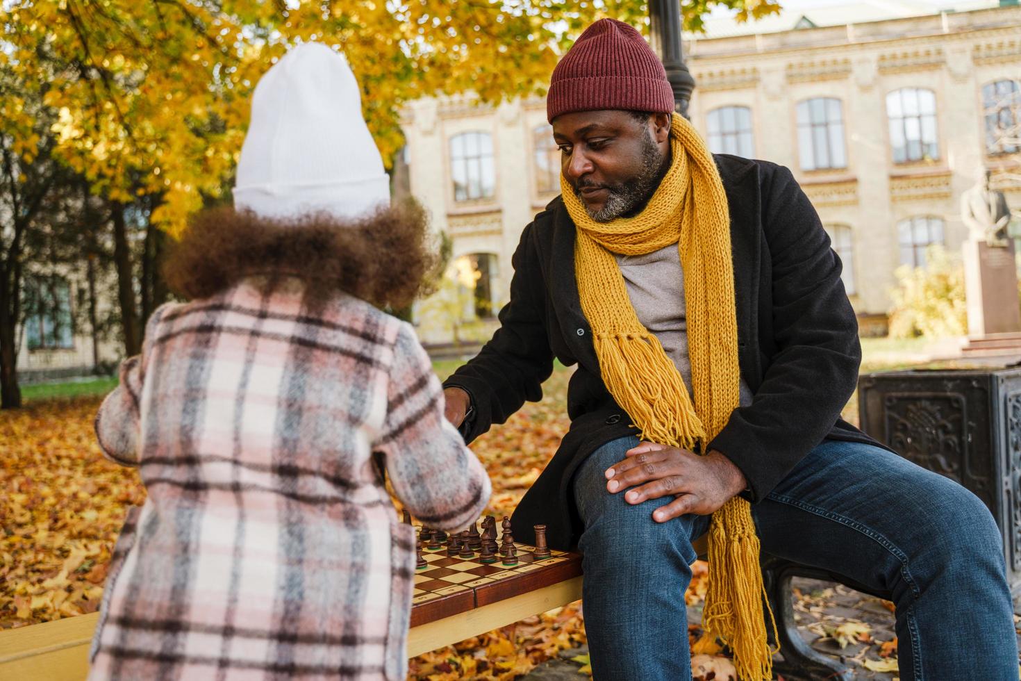 Abuelo y nieta negros jugando al ajedrez en el parque de otoño foto