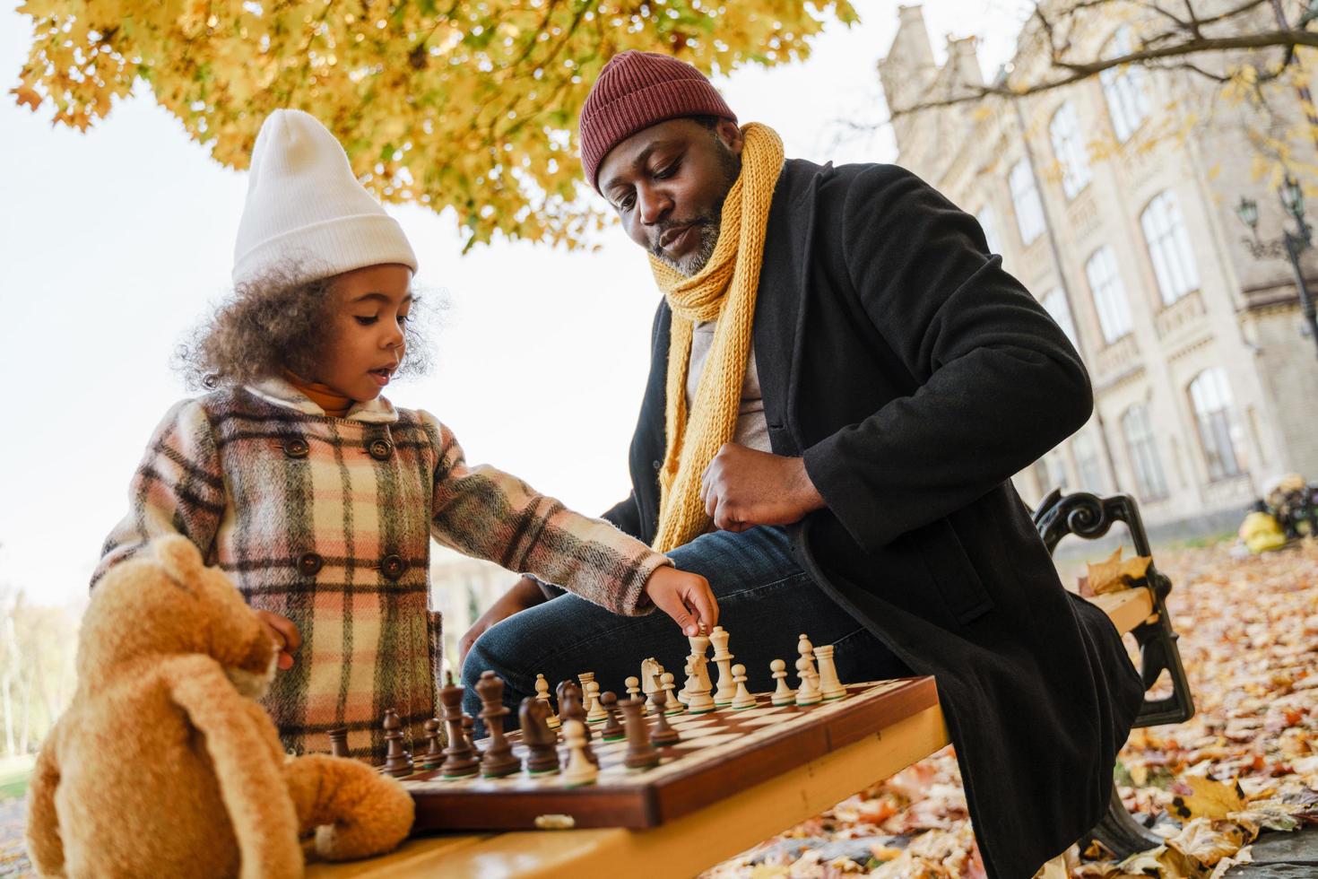 Abuelo y nieta negros jugando al ajedrez en el parque de otoño foto
